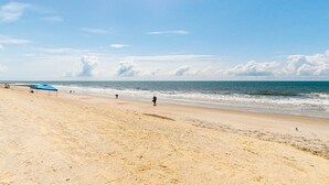 Ein Strand mit blauem Zelt, klarem Himmel und wenigen Personen.