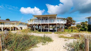 Ein Strandgrundstück mit einer Holzterrasse, einem überdachten Gang und einem Sandweg, der zum Eingang führt.