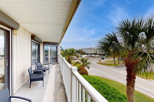 A balcony with chairs, a view of a road, and palm trees.