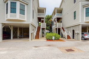 A residential building with a garage, a staircase, and a small garden area. - Top-floor 3rd-row condo with balcony, AC, outdoor pool & beach access (Edisto Beach)