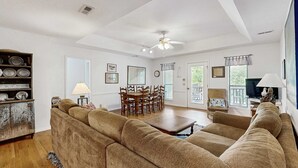 A living room with a sofa, dining table, chairs, and a television. - Steps to the Beach & Shops Home on a Tidal Creek w/ Two Decks, AC & WiFi (Edisto Beach)