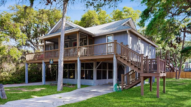 A two-story house with a balcony, a covered porch, and a staircase leading to the upper level. - Steps to the Beach & Shops Home on a Tidal Creek w/ Two Decks, AC & WiFi (Edisto Beach)