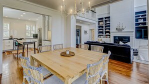 Un'ampia sala da pranzo con tavolo in legno e sedie in vimini, un lampadario e un caminetto decorato con un motivo nautico.