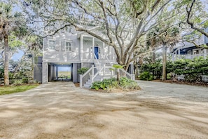 A large, two-story house with a porch and a staircase leading to the entrance. - Wonderful coastal home with ocean & creek views, Ping-Pong table, & dock (Edisto Island)