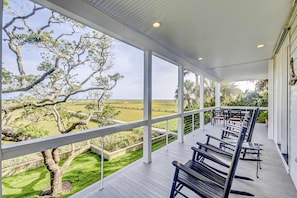 A covered outdoor area with a view of a grassy field and trees. - Wonderful coastal home with ocean & creek views, Ping-Pong table, & dock (Edisto Island)