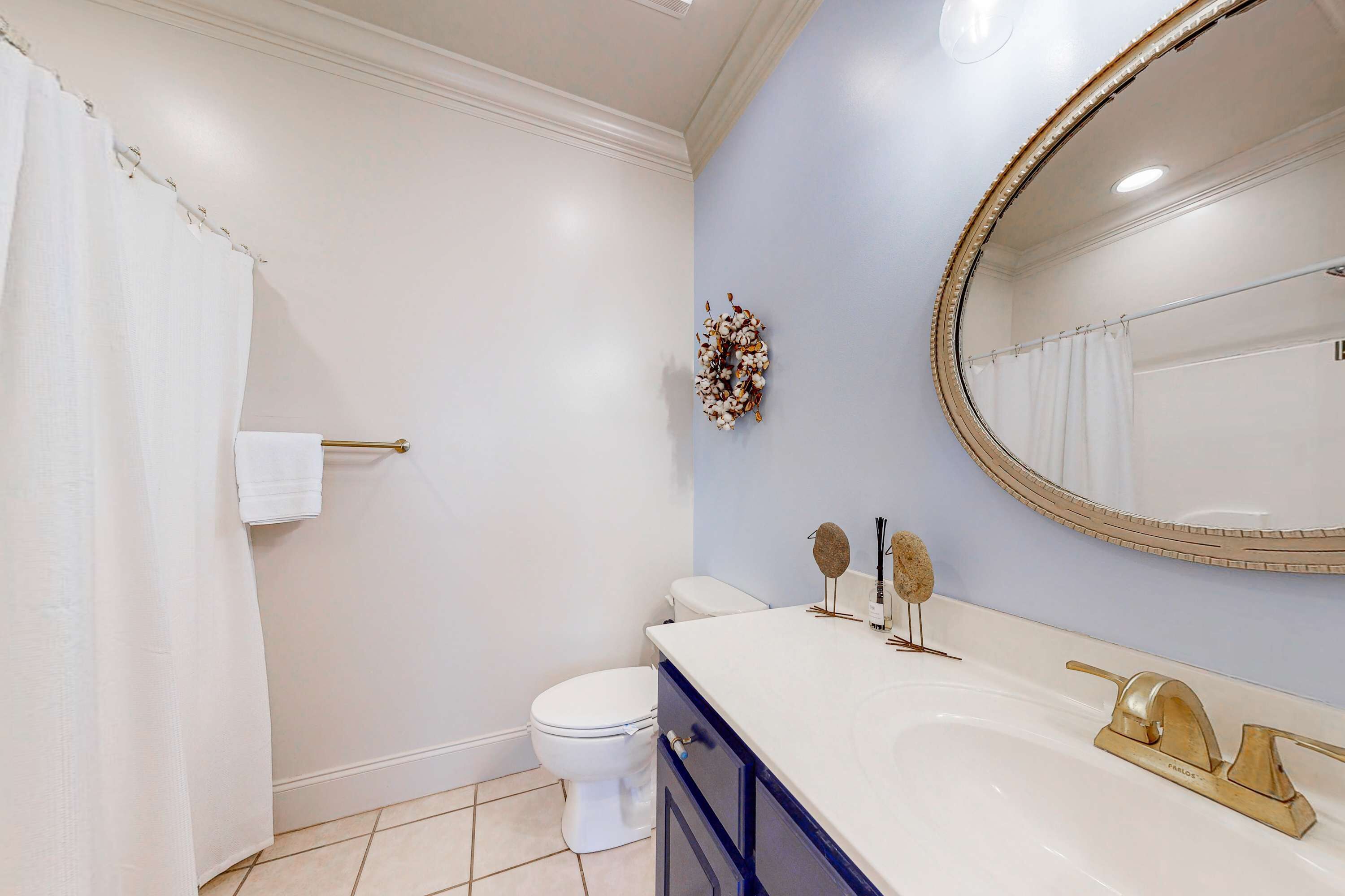 A bathroom with a toilet, a sink with a gold faucet, a mirror with a gold frame, and a towel rack.