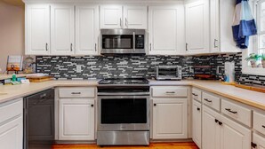 Uma cozinha com armários brancos, micro-ondas de aço inoxidável, forno embutido e torradeira.