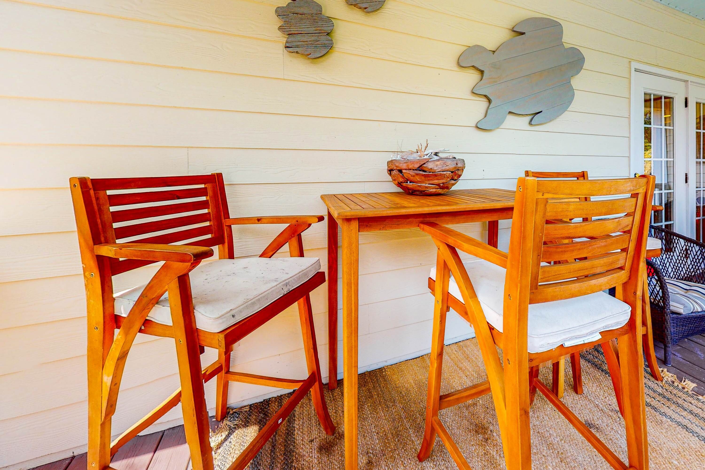 A wooden table and two chairs with a woven rug, a decorative wall piece, and a door with glass panels.