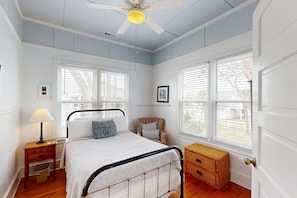 Ein Schlafzimmer mit Bett, Nachttisch, Lampe, Kommode und Fenster.