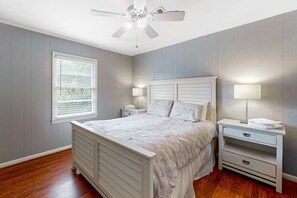 A bedroom with a bed, bedside tables, a ceiling fan, a window with blinds, and a nightstand with a lamp. - Lovely, Dog-Friendly House Close to Beach w/Free WiFi, Central AC, Private Pool (Edisto Beach)