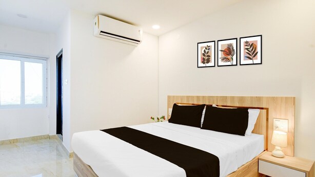 A modern hotel room with a large bed, a bedside table with a lamp, and a window with a view. - Suite Karmanghat Midtown (Hyderabad)