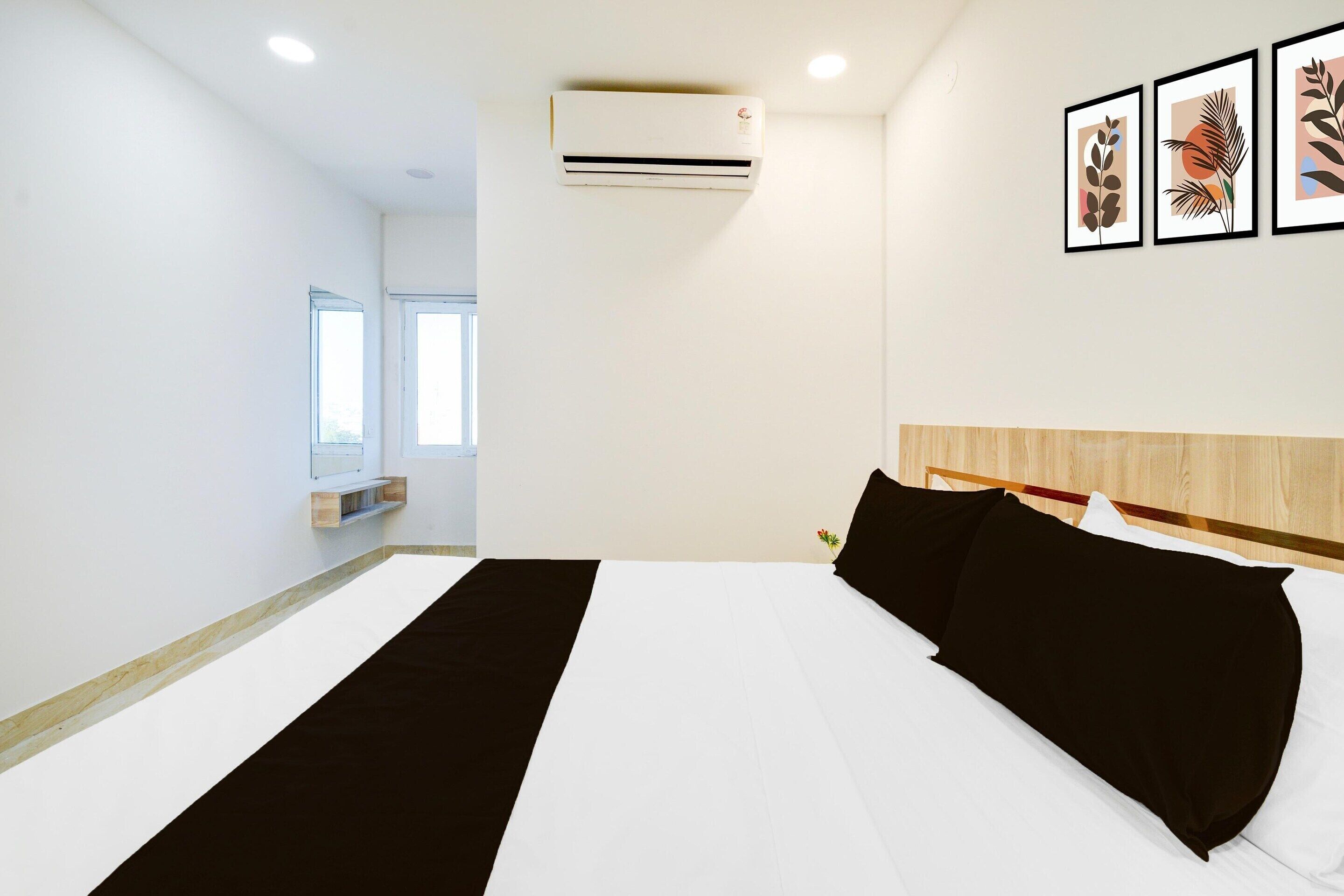 A hotel room with a bed, an air conditioner, a window, and a wall-mounted shelf.