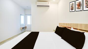 A hotel room with a bed, an air conditioner, a window, and a wall-mounted shelf.