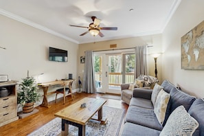 Ein Wohnzimmer mit Deckenventilator, Fernseher, Couchtisch aus Holz, Sofa und Schreibtisch mit Stuhl.