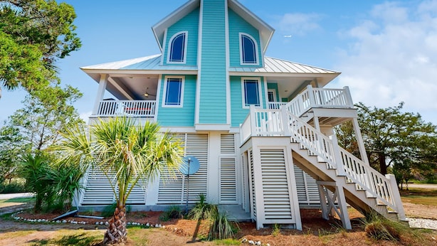 A large, two-story house with a steeply pitched roof, a balcony, and a staircase leading to the upper floor. - Coastal home- Marsh Views with open floor plan and stunning sunsets (Edisto Island)