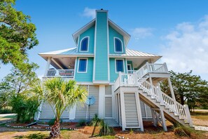 A large, two-story house with a steeply pitched roof, a balcony, and a staircase leading to the upper floor. - Coastal home- Marsh Views with open floor plan and stunning sunsets (Edisto Island)