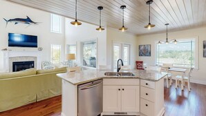 A spacious kitchen with a central island, a dining area with white chairs, a fireplace, and a mounted fish. - Coastal home- Marsh Views with open floor plan and stunning sunsets (Edisto Island)
