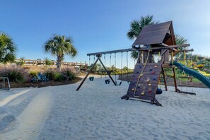 A playground with a swing set and climbing wall, surrounded by sand and palm trees. - Oceanfront villa with WiFi, full kitchen, pool, & hot tub - beach nearby (Hilton Head)