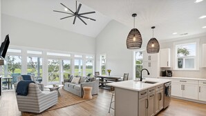 En rummelig opholdsstue med sofa, sofabord og spisebord, et køkken med hvide skabe og en stor ø, samt et loft med en lampe i stjerneform.
