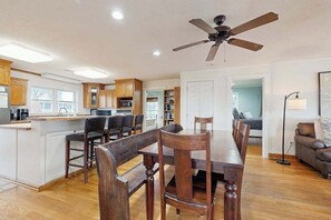 A spacious kitchen with wooden cabinets, a dining area with a large wooden table and chairs, a ceiling fan, and a view into the living room. - Enchanting & sunlit dog-friendly retreat with generous deck - steps to the sand (Edisto Beach)