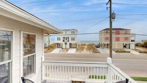 Una propiedad frente a la playa con un porche, vista a la playa y un edificio de varios pisos al fondo.
