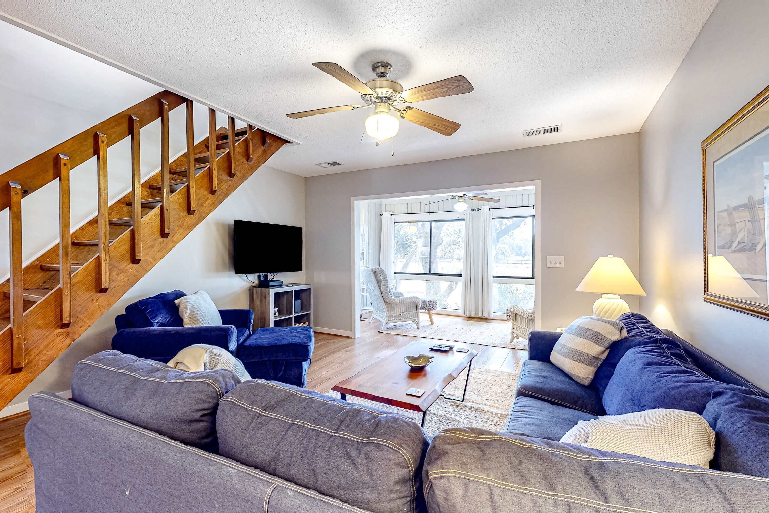 A living room with a wooden staircase, a ceiling fan, a sofa, a coffee table, and a television.