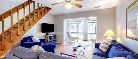 A living room with a wooden staircase, a ceiling fan, a sofa, a coffee table, and a television.
