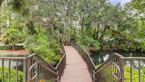 A wooden bridge with metal railings, surrounded by lush greenery and trees. - Newly renovated villa near the beach with pool & tennis  walk to Coligny Plaza (Hilton Head)