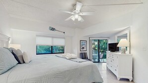 A bedroom with a bed, a ceiling fan, a TV, a dresser, and a window with a view. - Newly renovated villa near the beach with pool & tennis  walk to Coligny Plaza (Hilton Head)