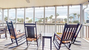 A covered outdoor area with rocking chairs, a table, and a ceiling fan. - Beautiful home across from the sea with balcony & open layout - dog-friendly (Edisto Beach)