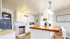A modern kitchen with white cabinetry, a wooden island, stainless steel appliances, and a framed marine life poster. - Beautiful home across from the sea with balcony & open layout - dog-friendly (Edisto Beach)