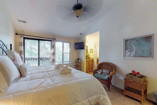 Una camera da letto con un letto grande, una televisione, una poltrona in vimini, un quadro e un balcone.