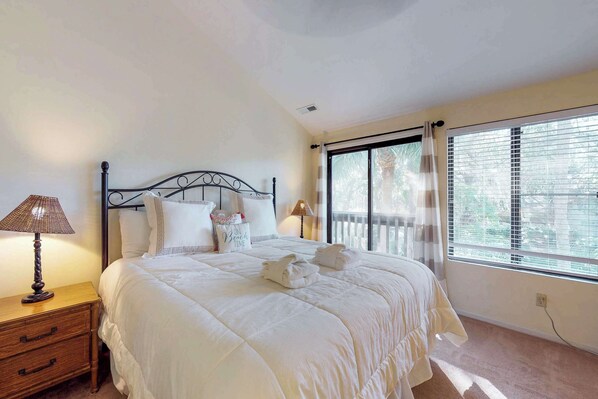 A neatly made bed with white bedding, a bedside table with a lamp, and a window with blinds. - Dog-Friendly Townhouse with Shared Pool, Easy Beach Access, and Golf (Hilton Head)