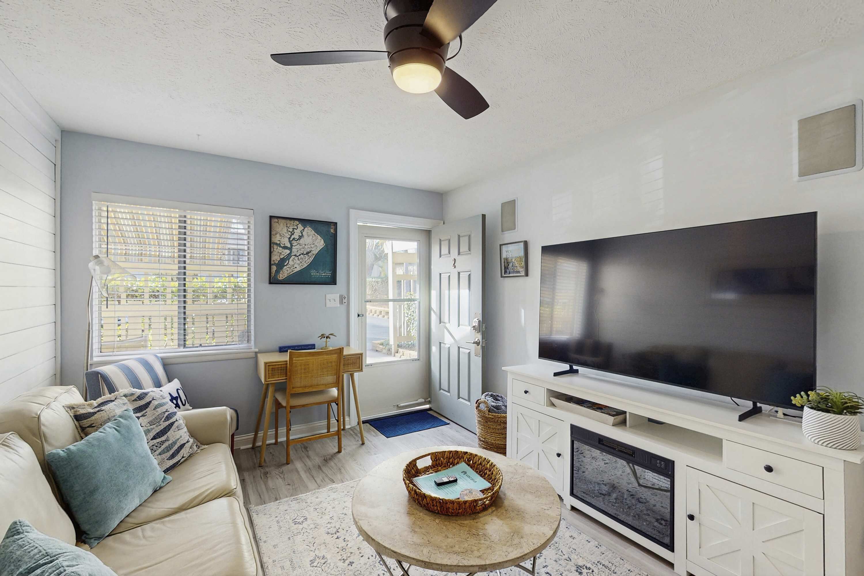 A living room with a sofa, TV, ceiling fan, and a door leading to the outside.
