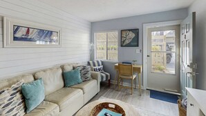 Una sala de estar acogedora con un sofá color beige, una silla a rayas, un escritorio de madera y una puerta que da al exterior.