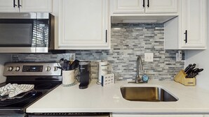 Una cocina con gabinetes blancos, un microondas de acero inoxidable, una cafetera y un fregadero.