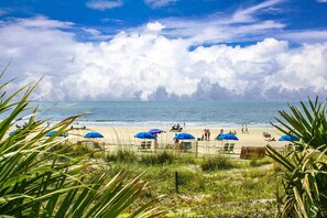 Ein Strand mit blauen Sonnenschirmen, Personen und einem Holzzaun.