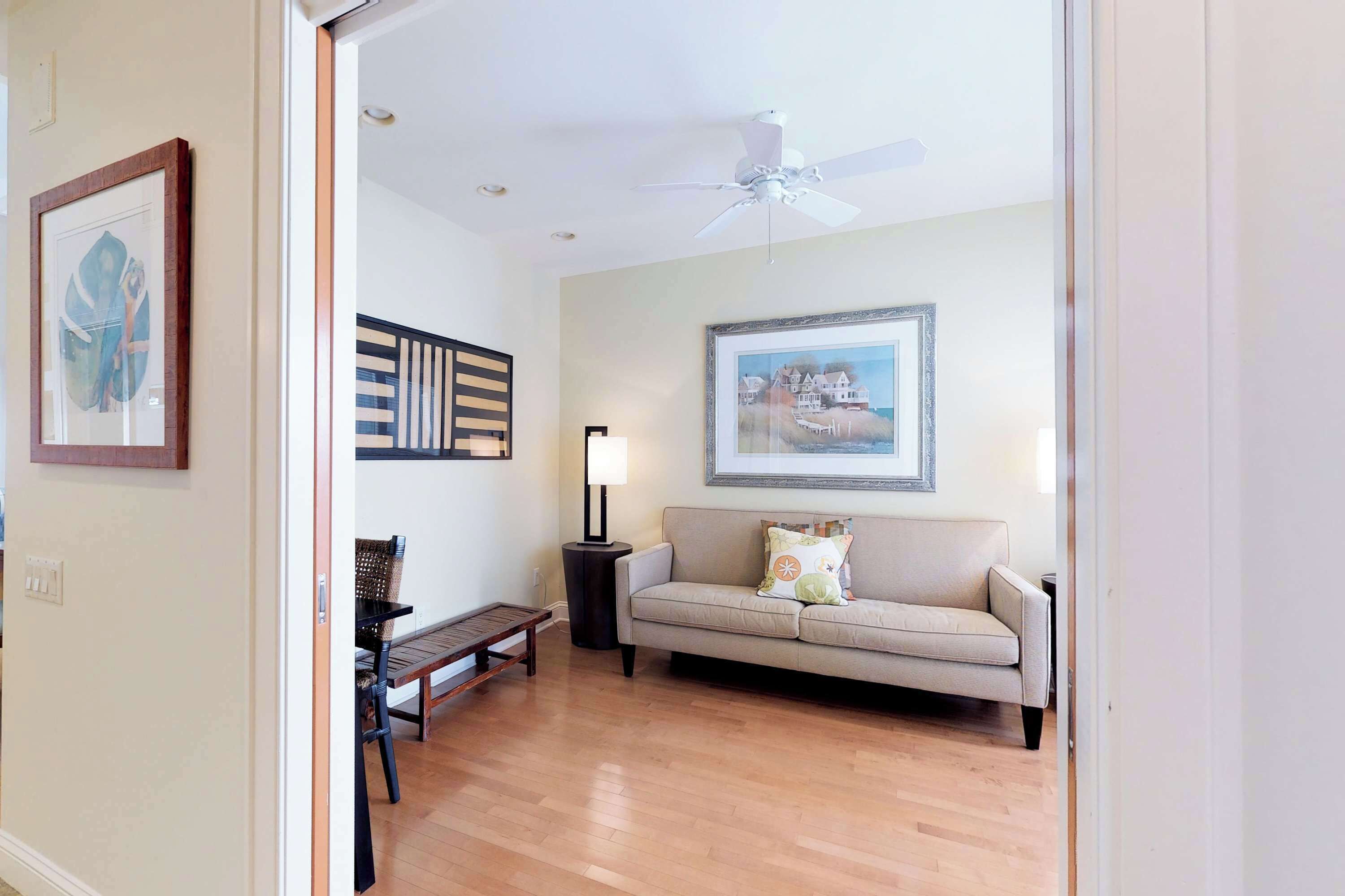 A living room with a sofa, a lamp, a ceiling fan, and framed artwork on the walls.