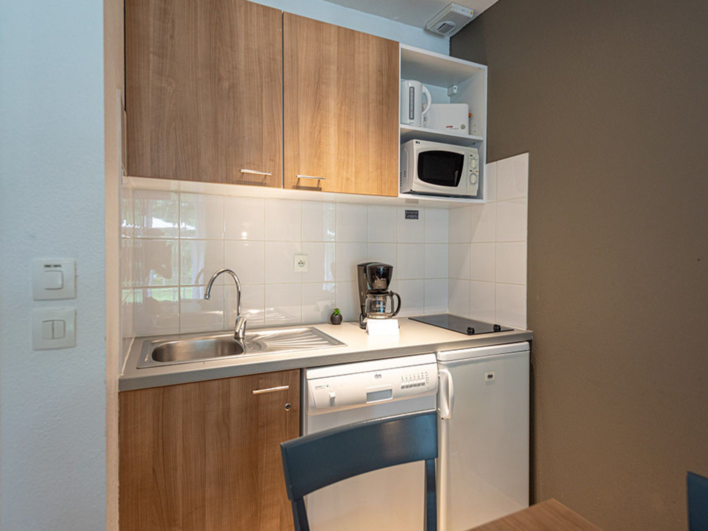 A compact kitchen with wooden cabinets, a microwave, a coffee maker, and a dishwasher.