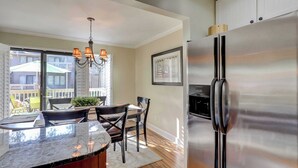A kitchen with a stainless steel refrigerator, a chandelier, and a dining area with chairs and a table. - Coastal Villa with Spacious Deck, Pool & Walk to Beach (Hilton Head)
