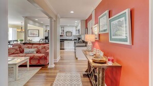 A modern living room with a sofa, a coffee table, and a kitchen in the background. - Coastal Villa with Spacious Deck, Pool & Walk to Beach (Hilton Head)