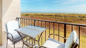 Ein Balkon mit Tisch und zwei Stühlen mit Blick auf eine Küstenlandschaft.