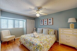 Une chambre à coucher comprenant un lit, une chaise, une commode, un ventilateur de plafond et des tableaux représentant des poissons accrochés au mur.