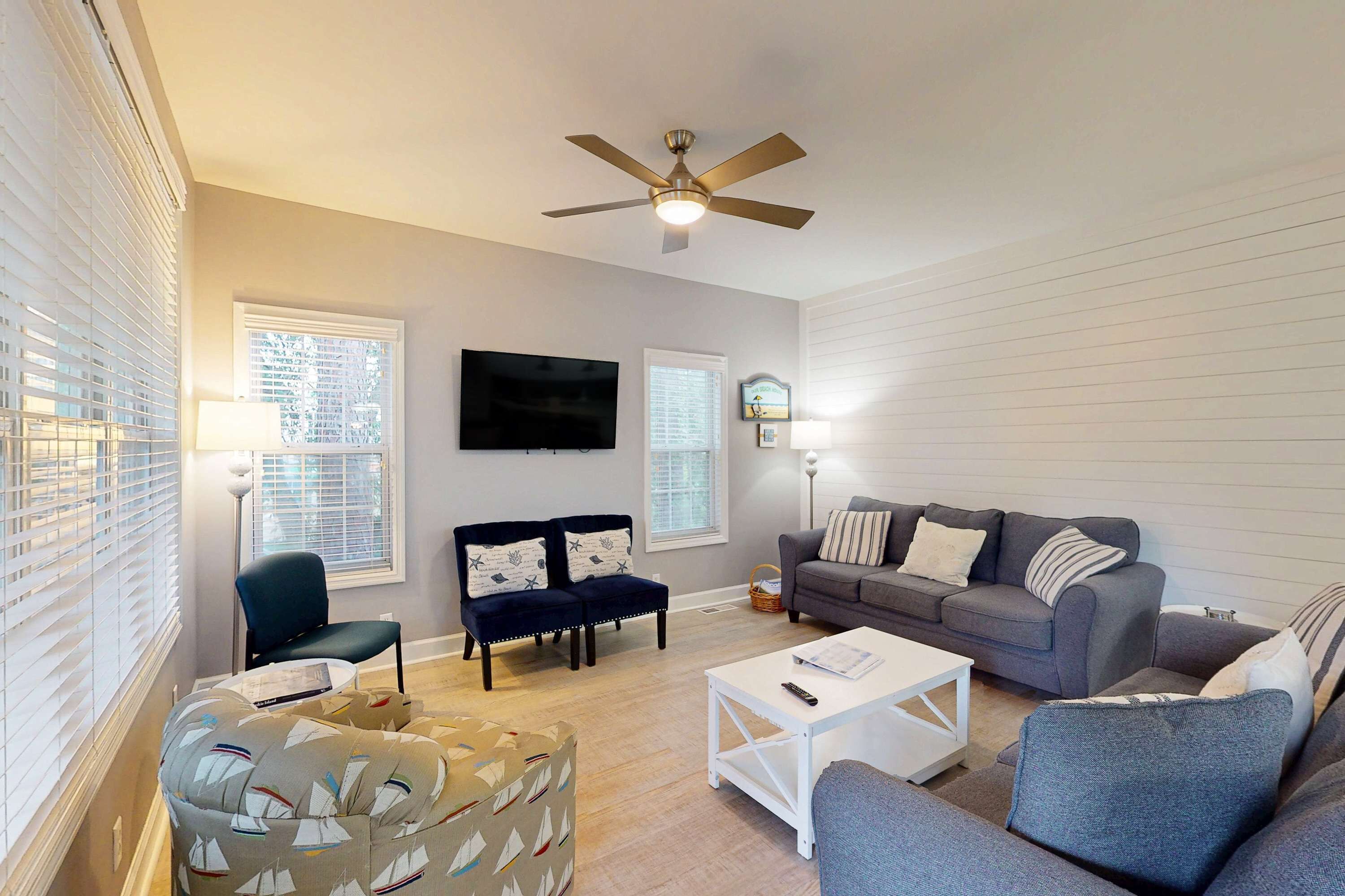 A living room with a ceiling fan, two armchairs, a sofa, a coffee table, and a television.