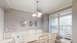 Una sala da pranzo con tavolo in legno e sedie bianche, un lampadario e tre specchi a parete.