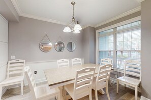 Ein Esszimmer mit Holztisch und weißen Stühlen, einer Kristallleuchter und drei Wandspiegeln.