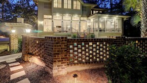 A two-story house with a large garage, a covered porch, and a brick wall with a decorative pattern. - Luxurious home with private pool, central AC, & high-speed WiFi - walk to beach (Hilton Head)