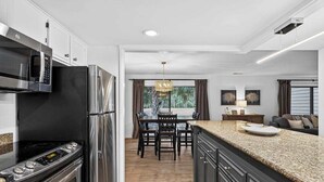A modern kitchen with stainless steel appliances, a dining area with a chandelier, and a view of the outdoors. - Charming Townhome with Golf Course View,On-site Pool and Short Walk to Beach! (Hilton Head)