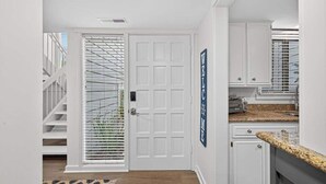 A hallway with a white door, a staircase, and a kitchen area with white cabinets and a granite countertop. - Charming Townhome with Golf Course View,On-site Pool and Short Walk to Beach! (Hilton Head)