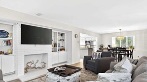 A living room with a flat-screen TV, a fireplace, a dining area, and a kitchen. - Charming Townhome with Golf Course View,On-site Pool and Short Walk to Beach! (Hilton Head)